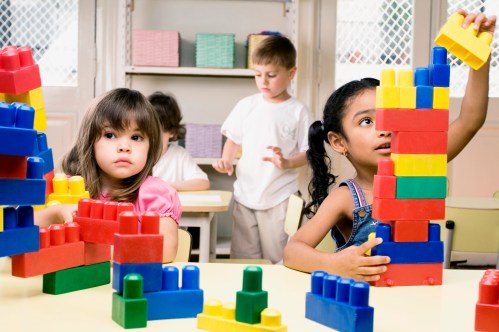 Two girls playing with plastic blocks with their friends in the background